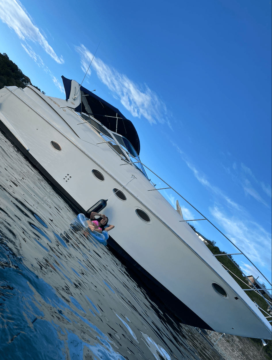 Person in a pink life jacket on a small boat near a large white yacht with a blue sky background.