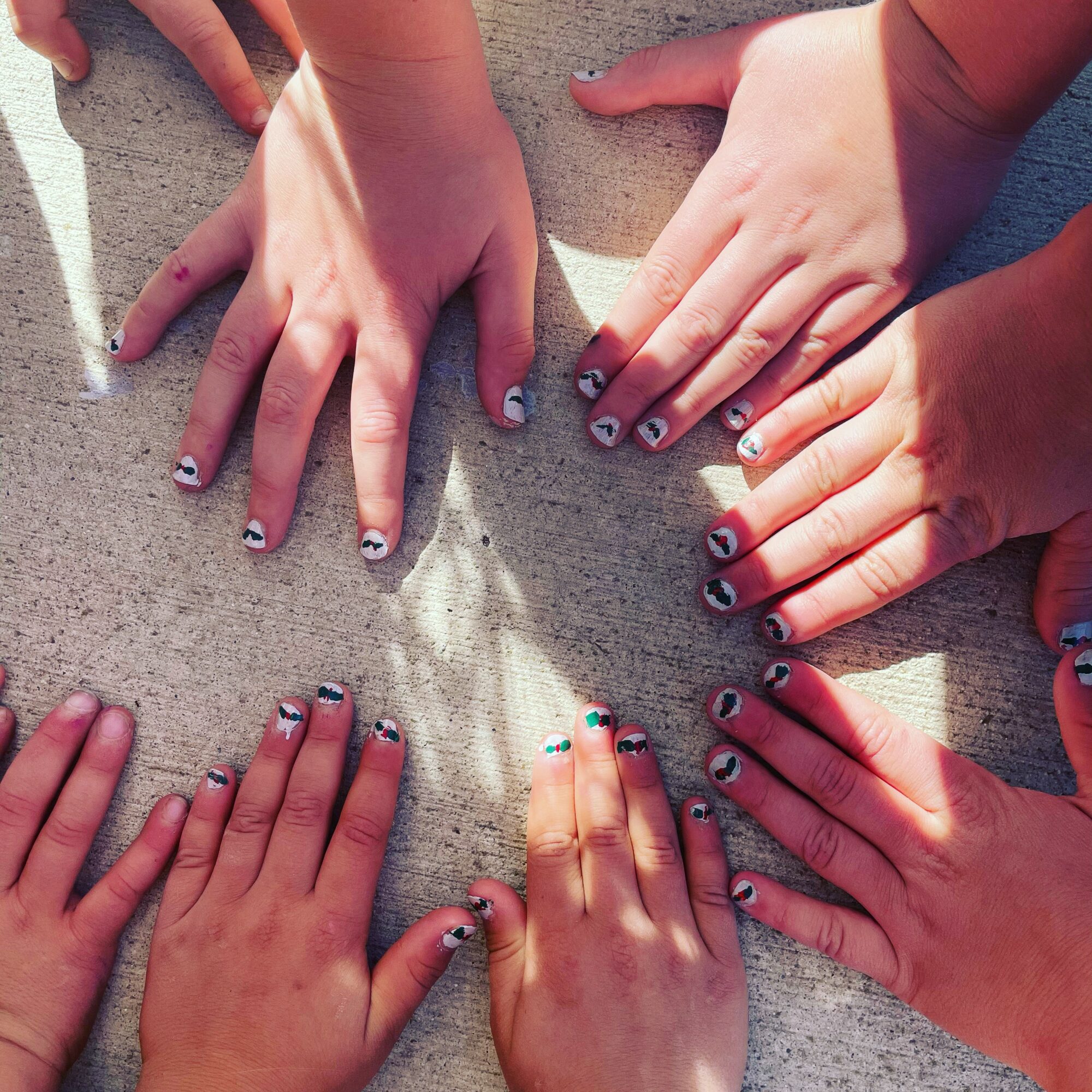 Six hands with painted nails placed on a concrete surface, showing diverse skin tones and nail designs.