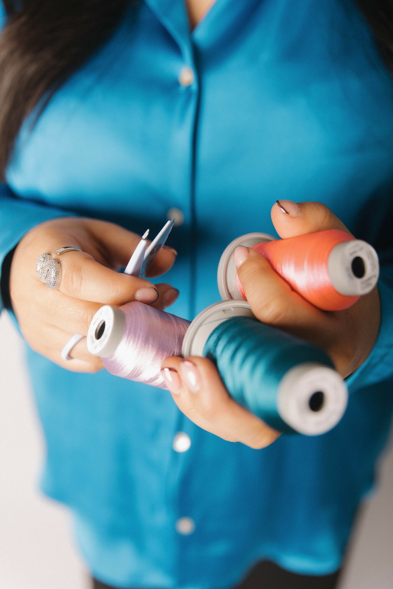 Person holding colorful spools of thread, wearing a blue shirt, with focus on hands and threads.