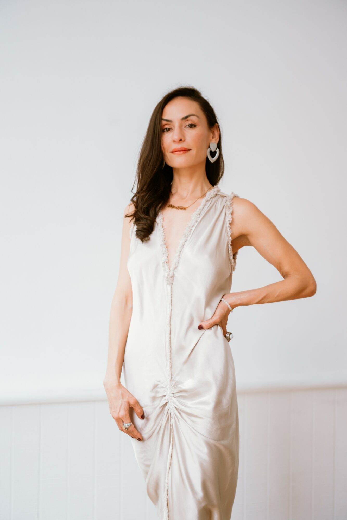 Woman in elegant dress with one hand on hip, standing against plain background.