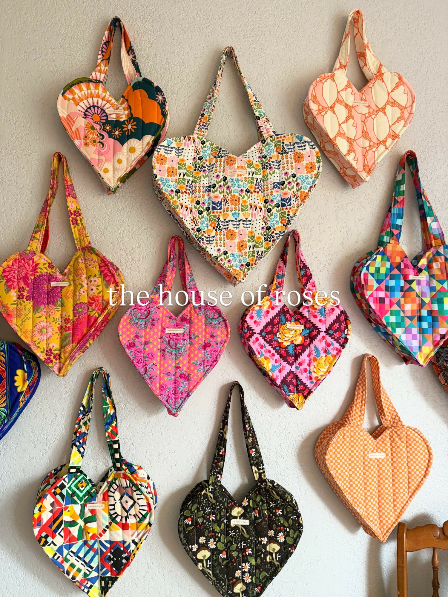 Collection of colorful fabric face masks hanging on a wall, various patterns and designs, some with floral and geometric motifs.