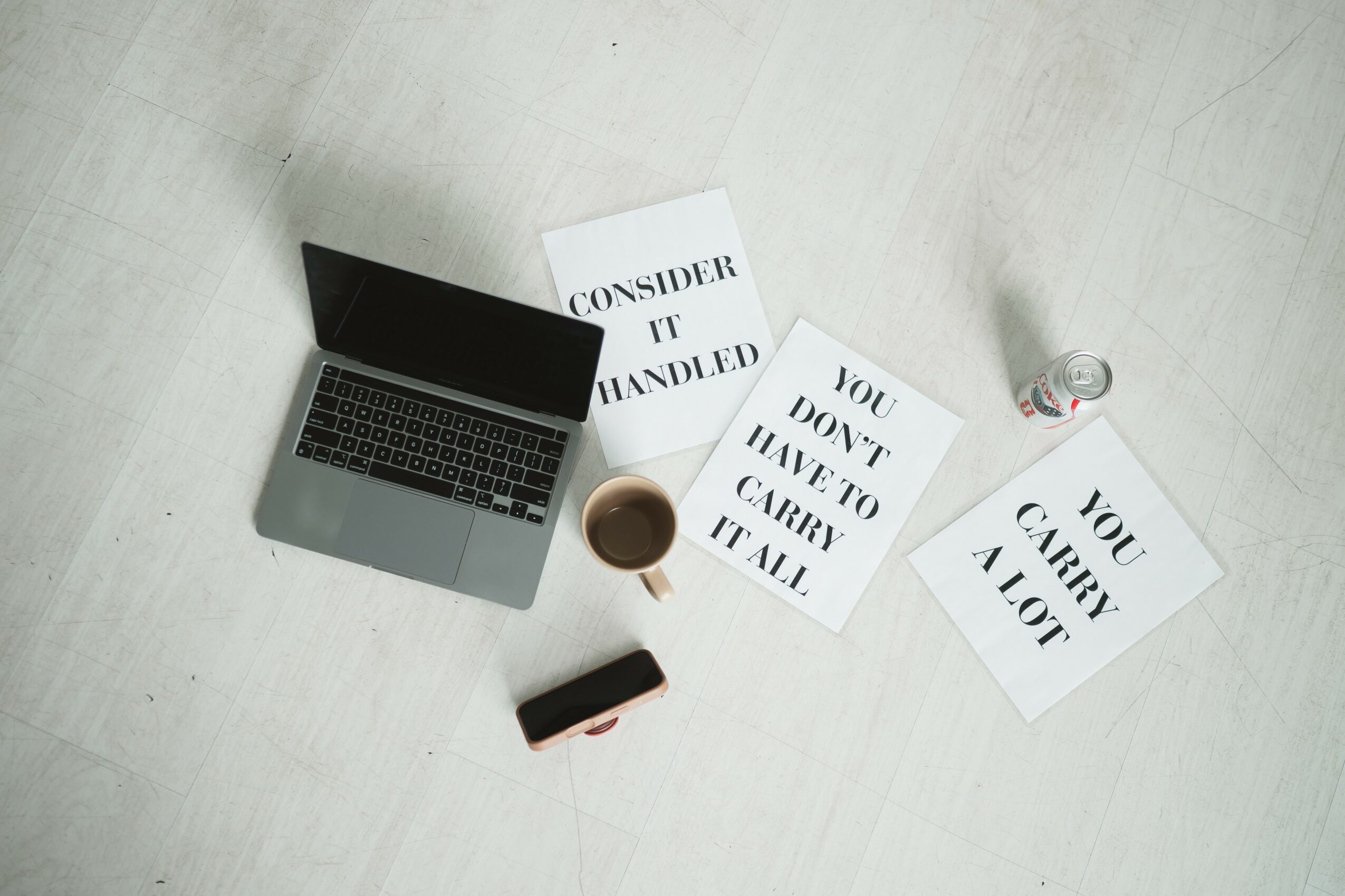 Laptop, coffee cup, phone, and papers on a light surface, with some papers partially under the laptop.