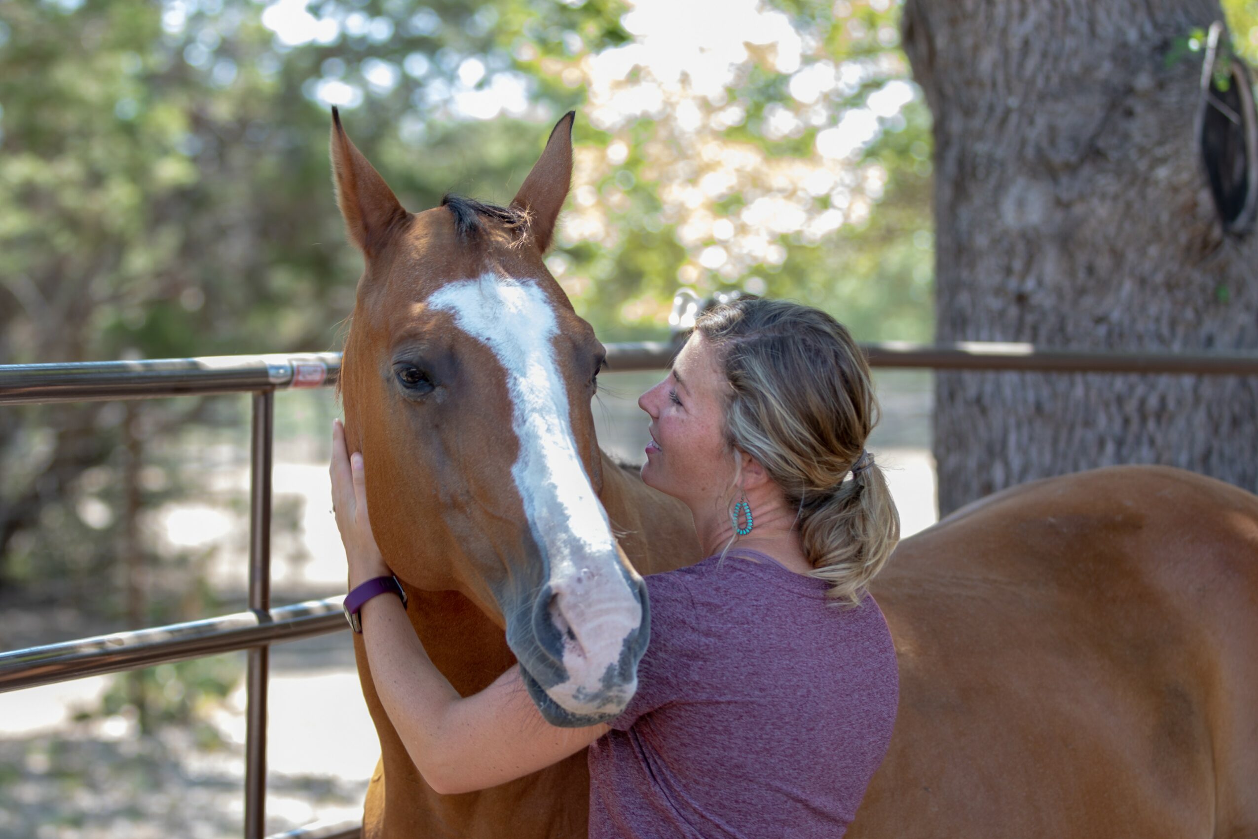 Woman hugging a brown horse with a white stripe on its face near a fence outdoors.