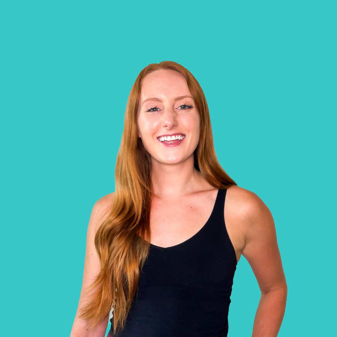 Smiling woman with long red hair wearing a black tank top against a teal background.