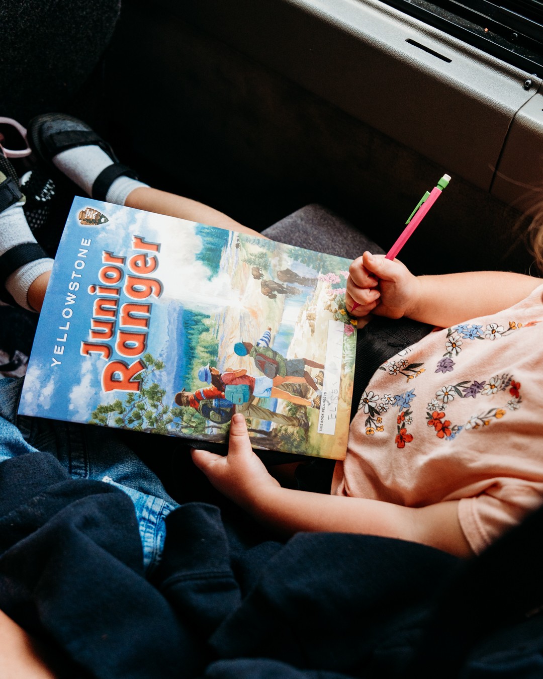Child holding a colorful book titled 'Jungle Ranger' with a pencil in hand, sitting on a bus seat.