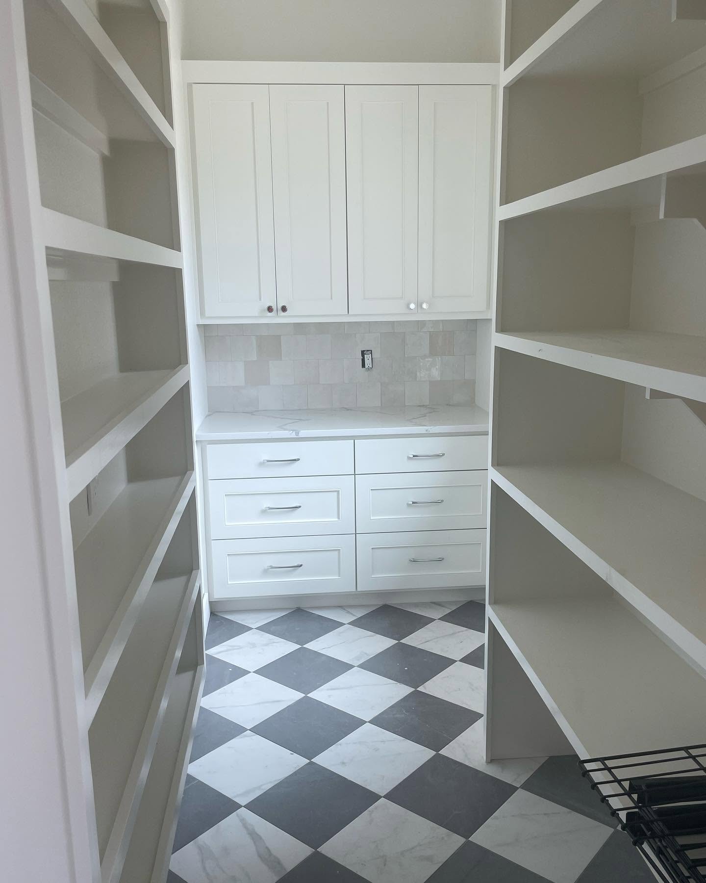View of a small pantry with white cabinets, shelves on both sides, and a black and white checkered floor.