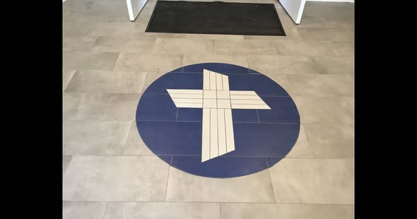 Floor circle with a cross symbol in the center, on a tiled floor near a door mat.