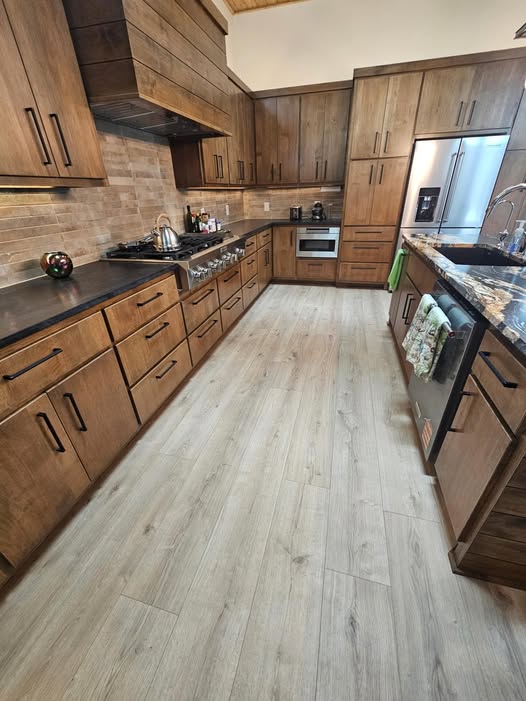Kitchen with wooden cabinets, black countertops, stainless steel appliances, and light-colored flooring.
