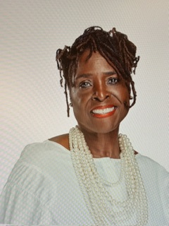 Portrait of a woman with short, styled hair, wearing a white top and layered pearl necklaces, smiling.