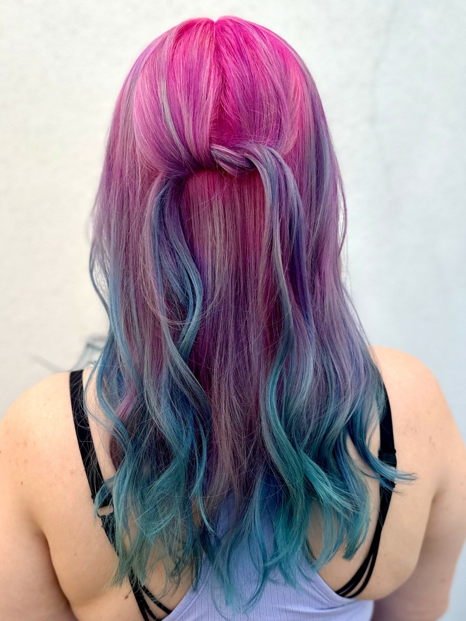 Back view of a person with long, wavy hair dyed in pink, purple, and blue shades.