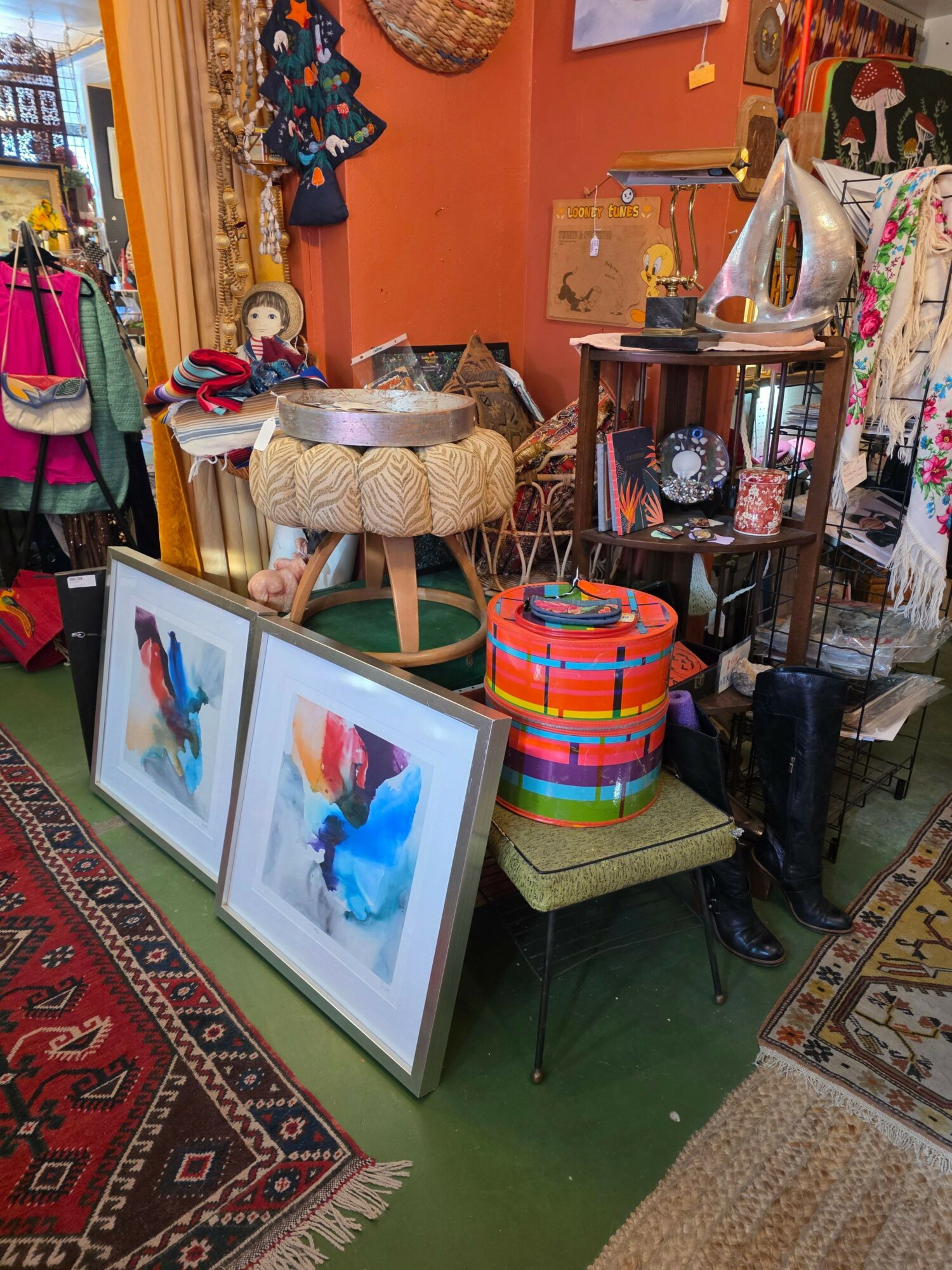 Room with colorful artwork, furniture, and decorative items, including framed paintings, a patterned rug, and various objects on shelves.