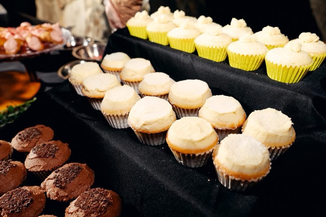 Assorted cupcakes and desserts displayed on black trays at a dessert table, with some cupcakes topped with white frosting.