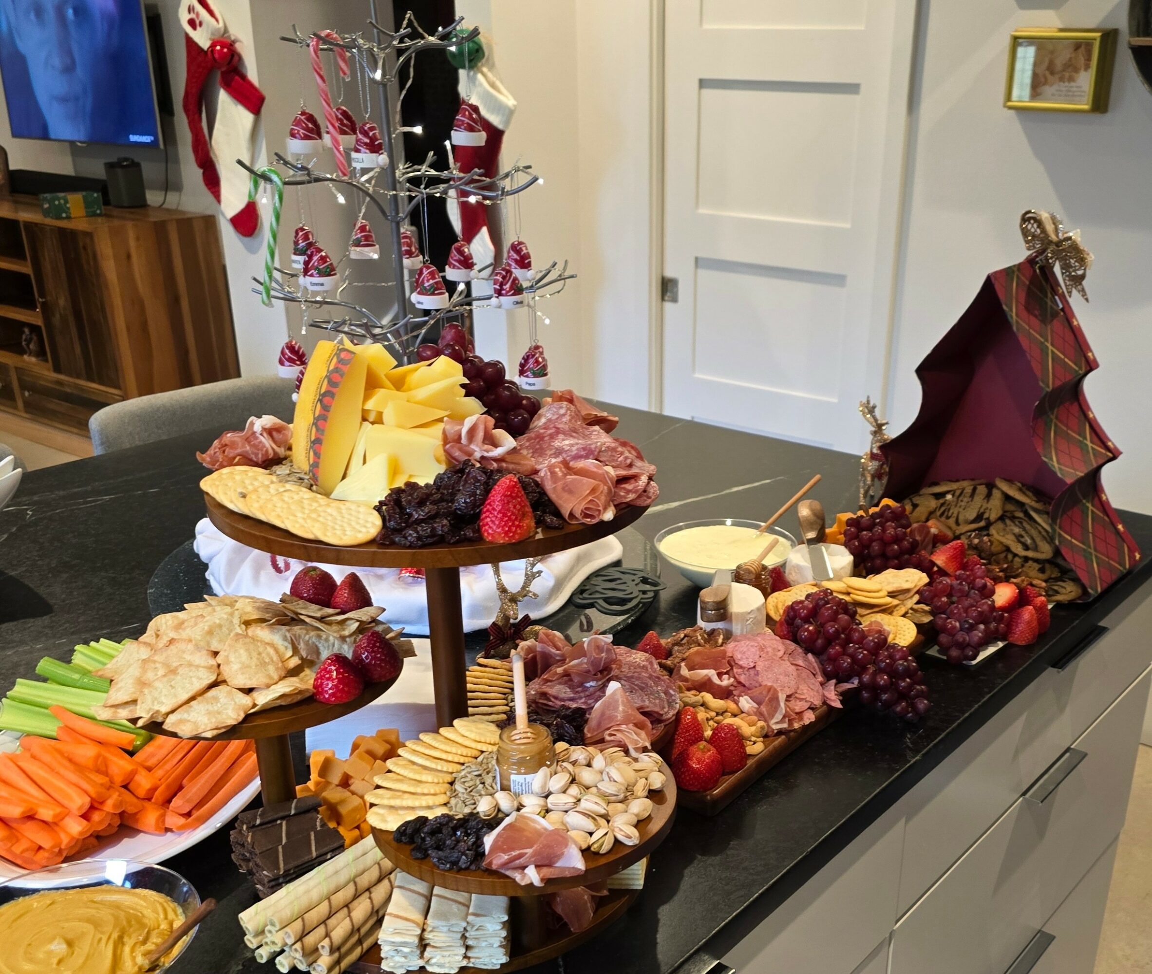 Festive holiday table with cheese, crackers, grapes, and meats, decorated with Christmas ornaments and a small Christmas tree in the background.
