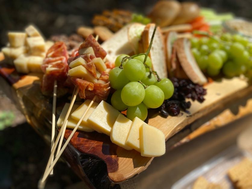Cheese, grapes, and assorted appetizers on a wooden platter, with skewers and various foods visible.