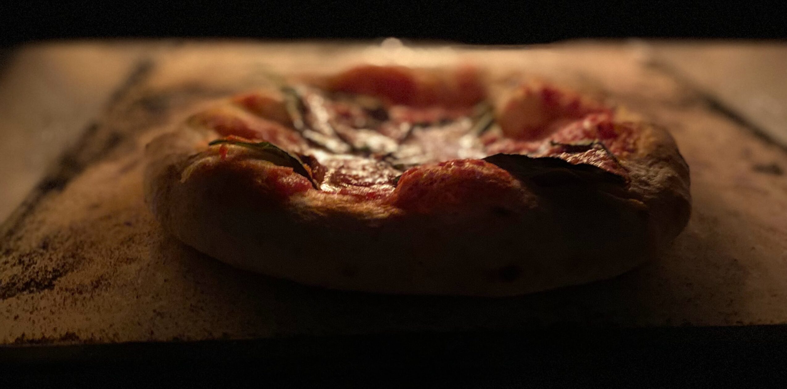 Pizza with toppings on a baking stone, viewed from above in dim lighting.