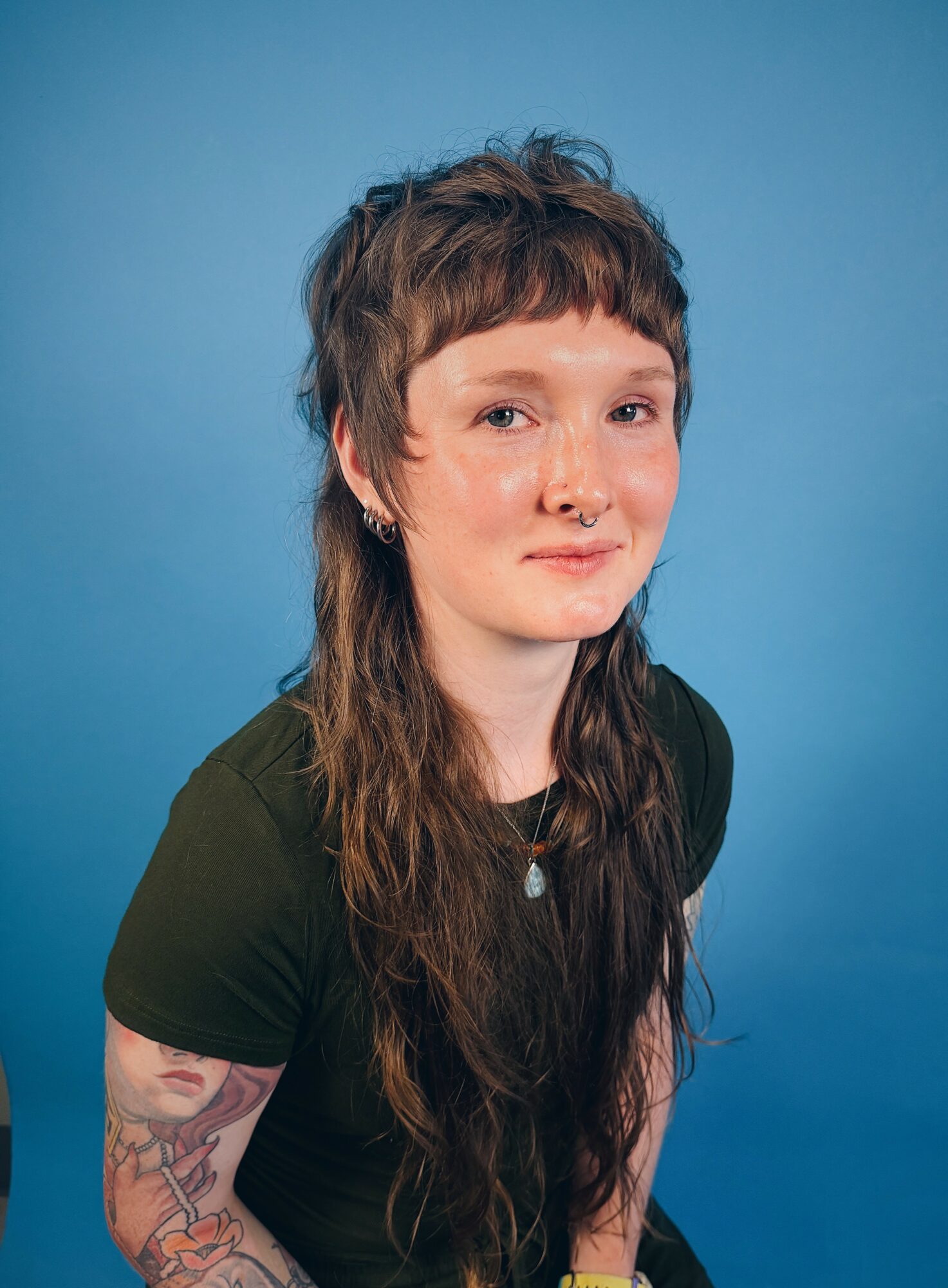Young woman with long wavy hair, wearing a black shirt and a necklace, smiling against a blue background.