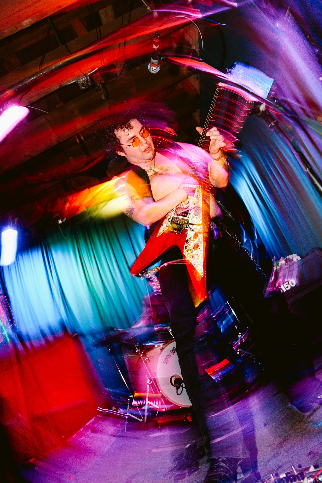 Performer on stage with colorful lights, holding a guitar, motion blur, vibrant atmosphere, energetic scene.