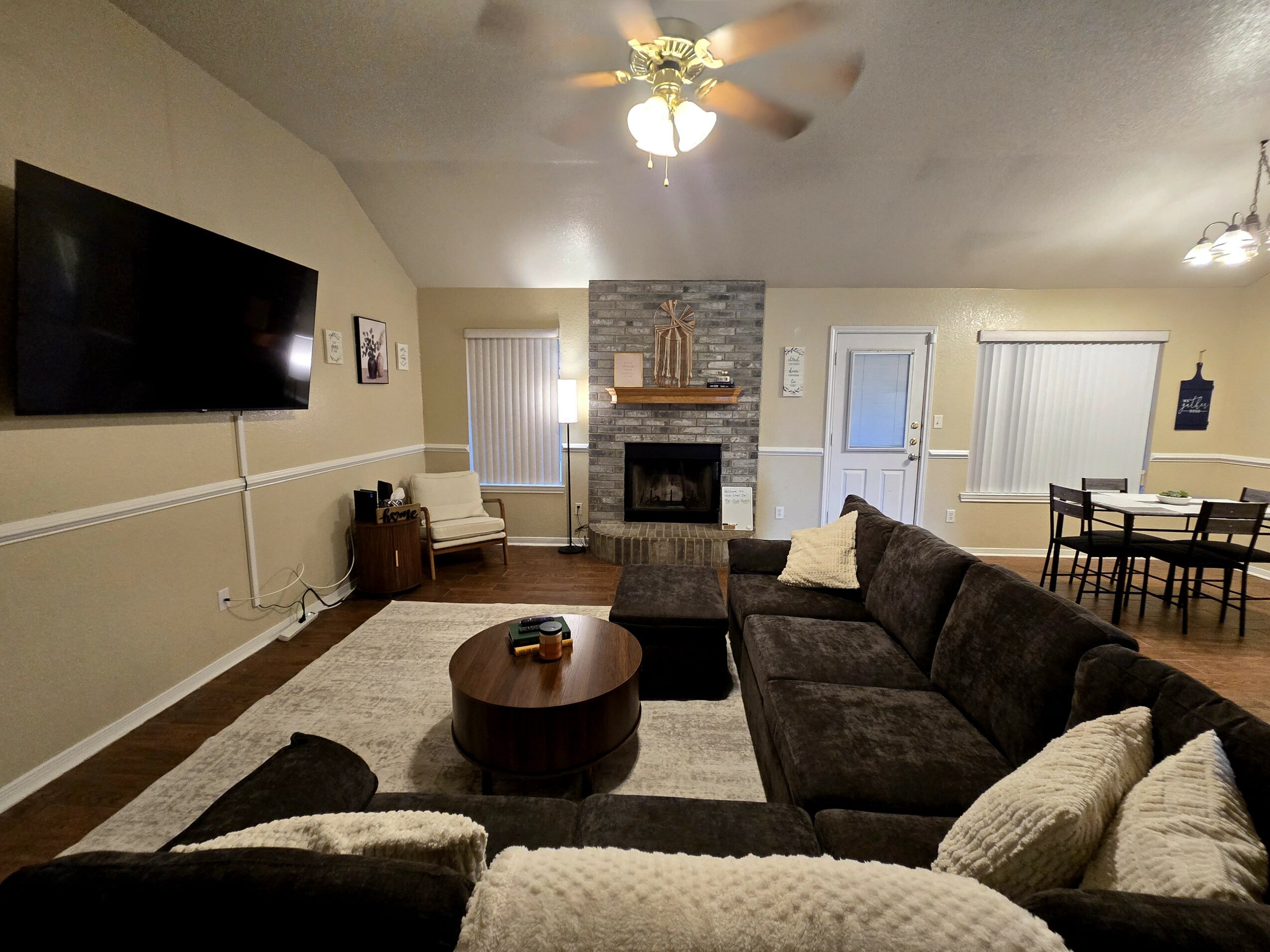 Living room with a large sectional sofa, fireplace, wall-mounted TV, and dining area in the background.