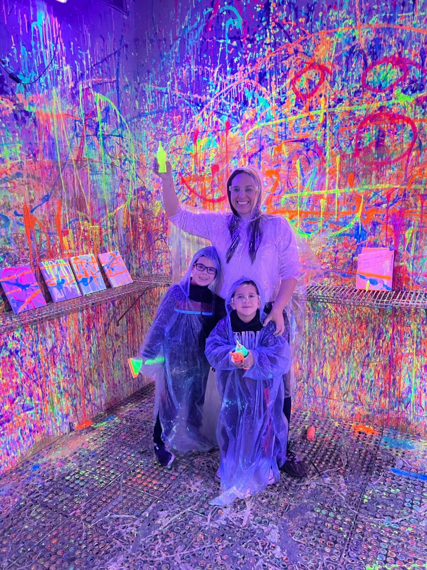 Two children in dark clothing stand in front of a colorful, graffiti-covered wall, with one child holding a toy or object. Word count: 20