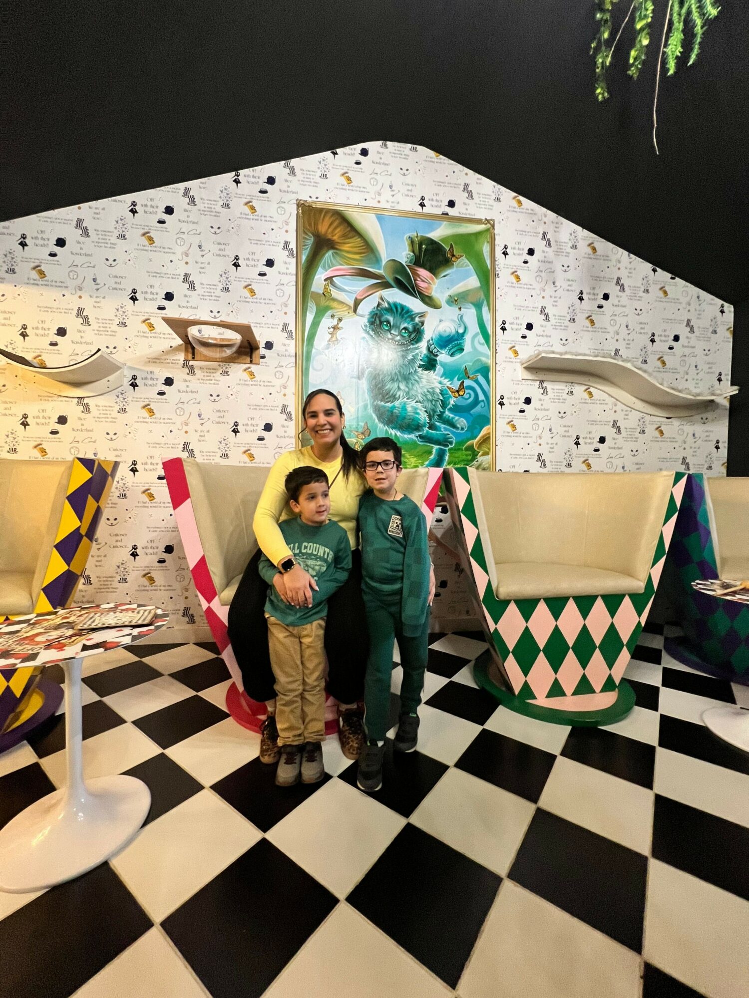 Three people stand in an art gallery with black and white checkered flooring, colorful artwork, and modern furniture.