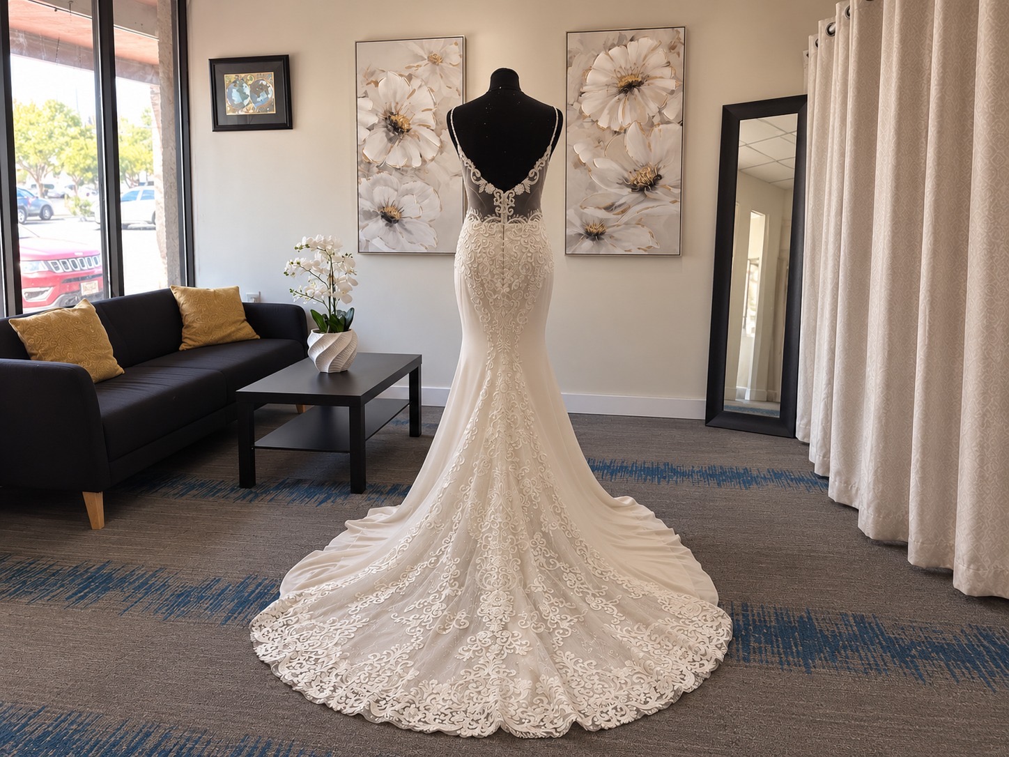 Elegant white wedding dress on a mannequin in a room with artwork, a mirror, and a sofa.