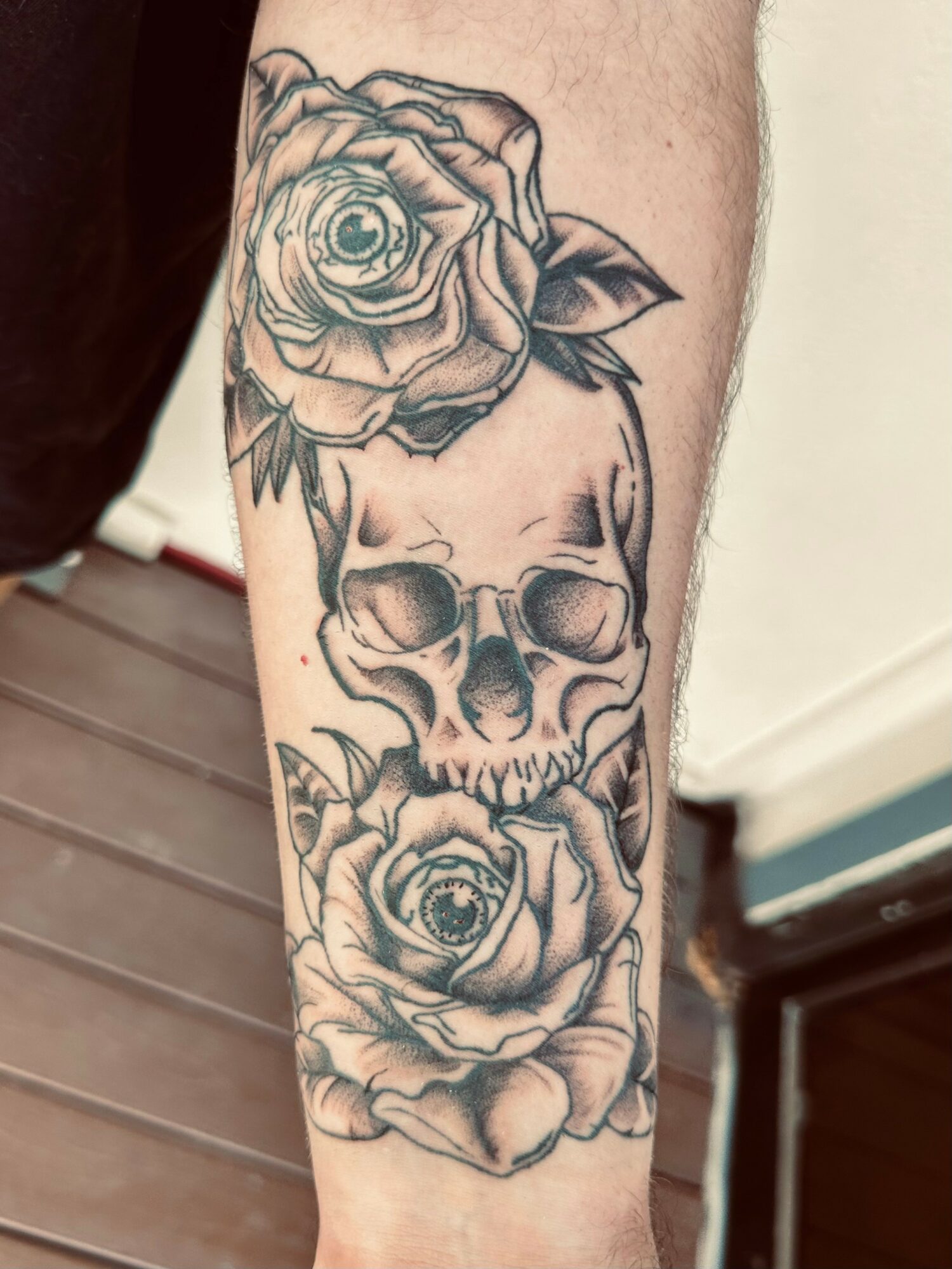 Tattoo of two skulls with roses, one above and one below, on a person's arm.