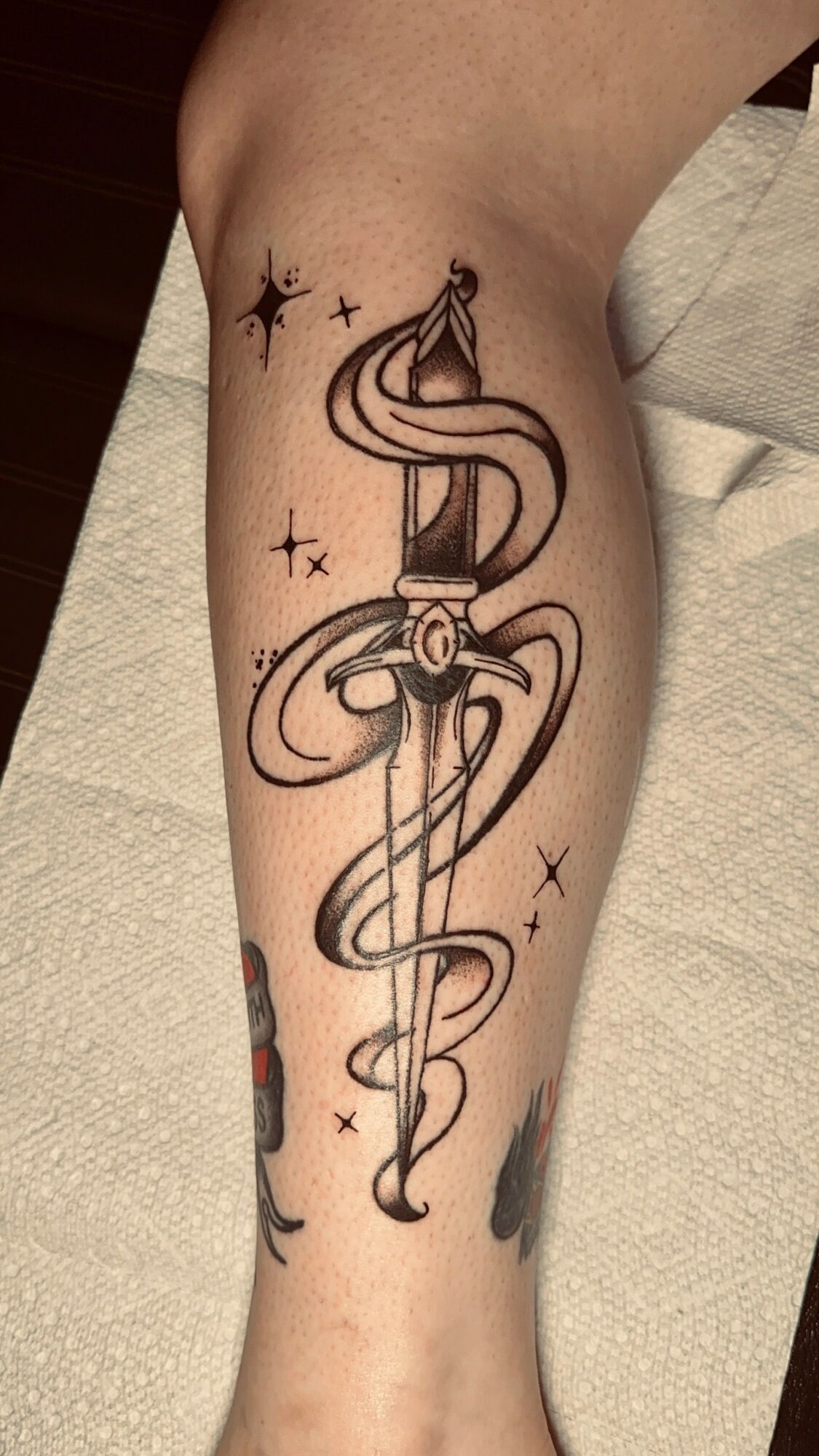 Tattoo of a caduceus symbol with a snake entwined around a staff, surrounded by stars, on a person's leg.