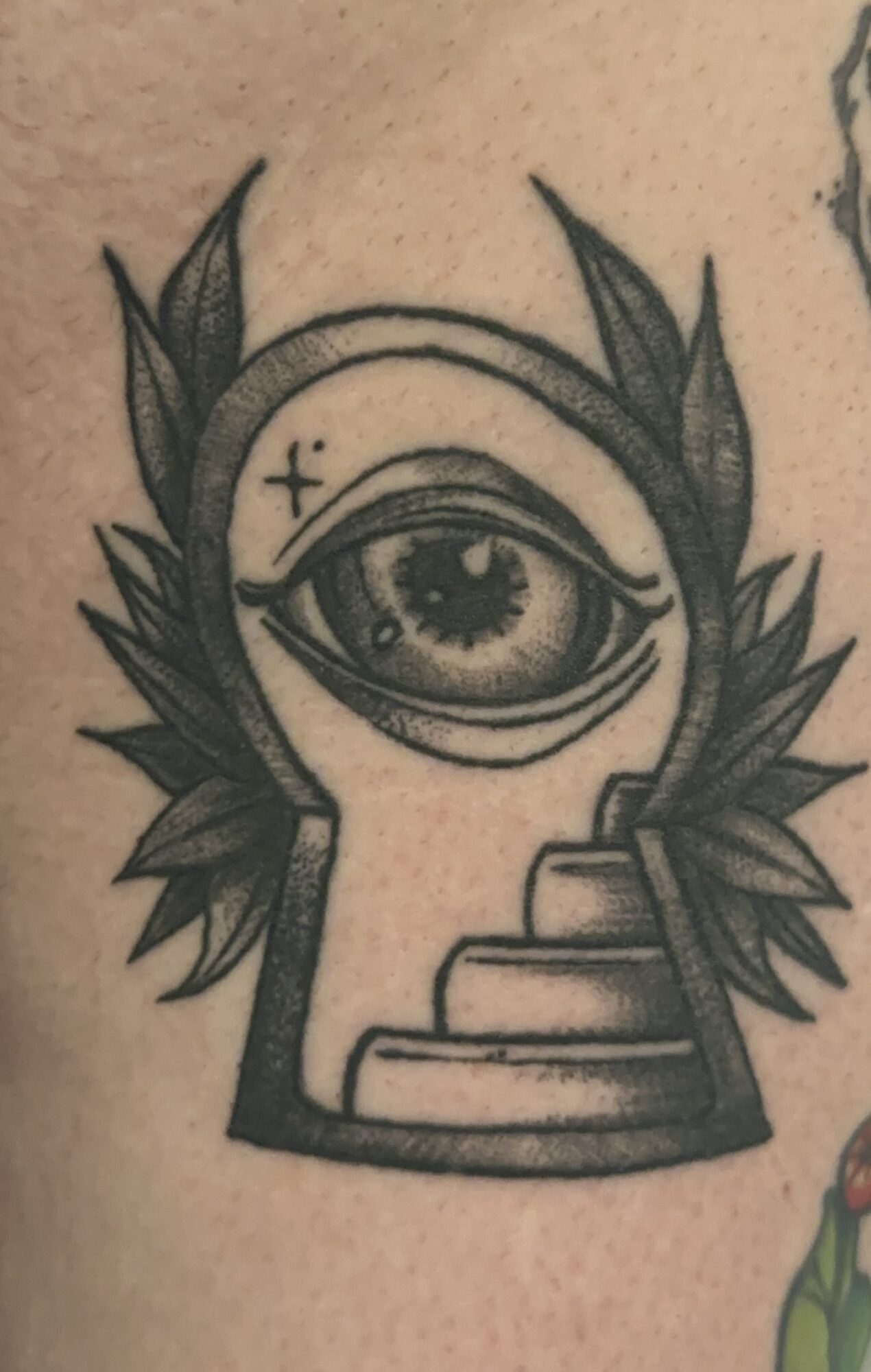 Tattoo of an eye with a staircase below, surrounded by leaves, in black ink.