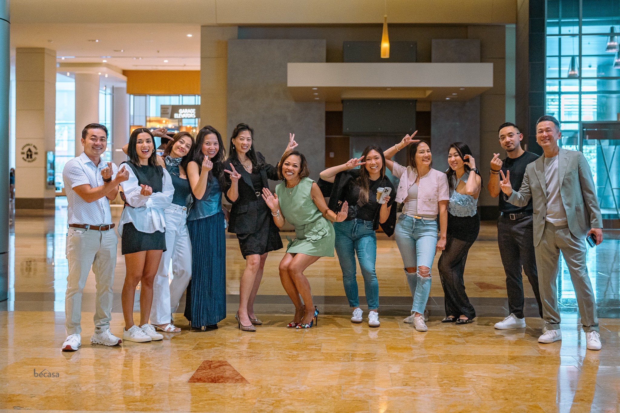 Group of ten people standing in a hotel lobby, smiling and waving at the camera.