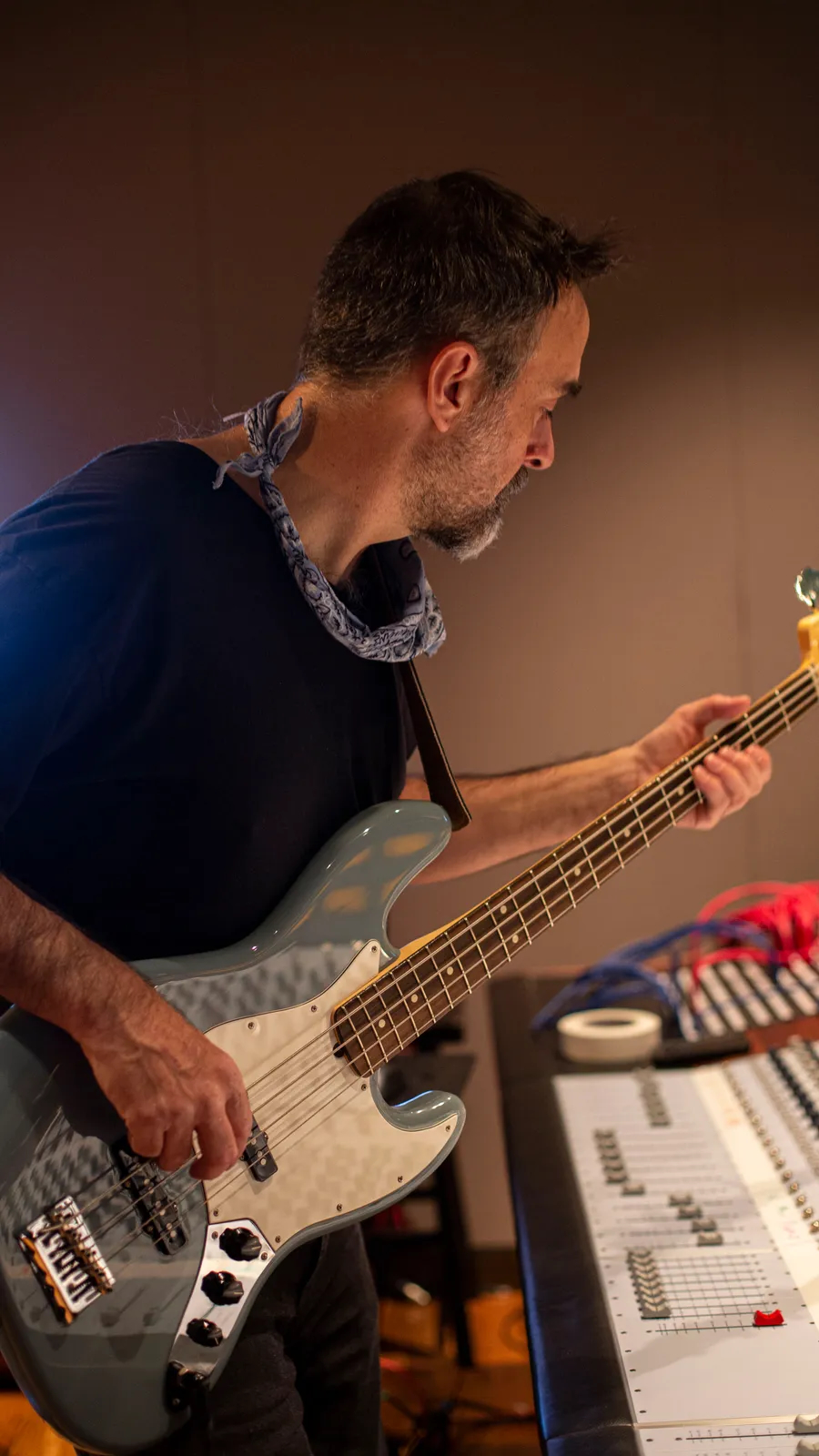 Man playing electric bass guitar in a music studio, with audio equipment nearby.