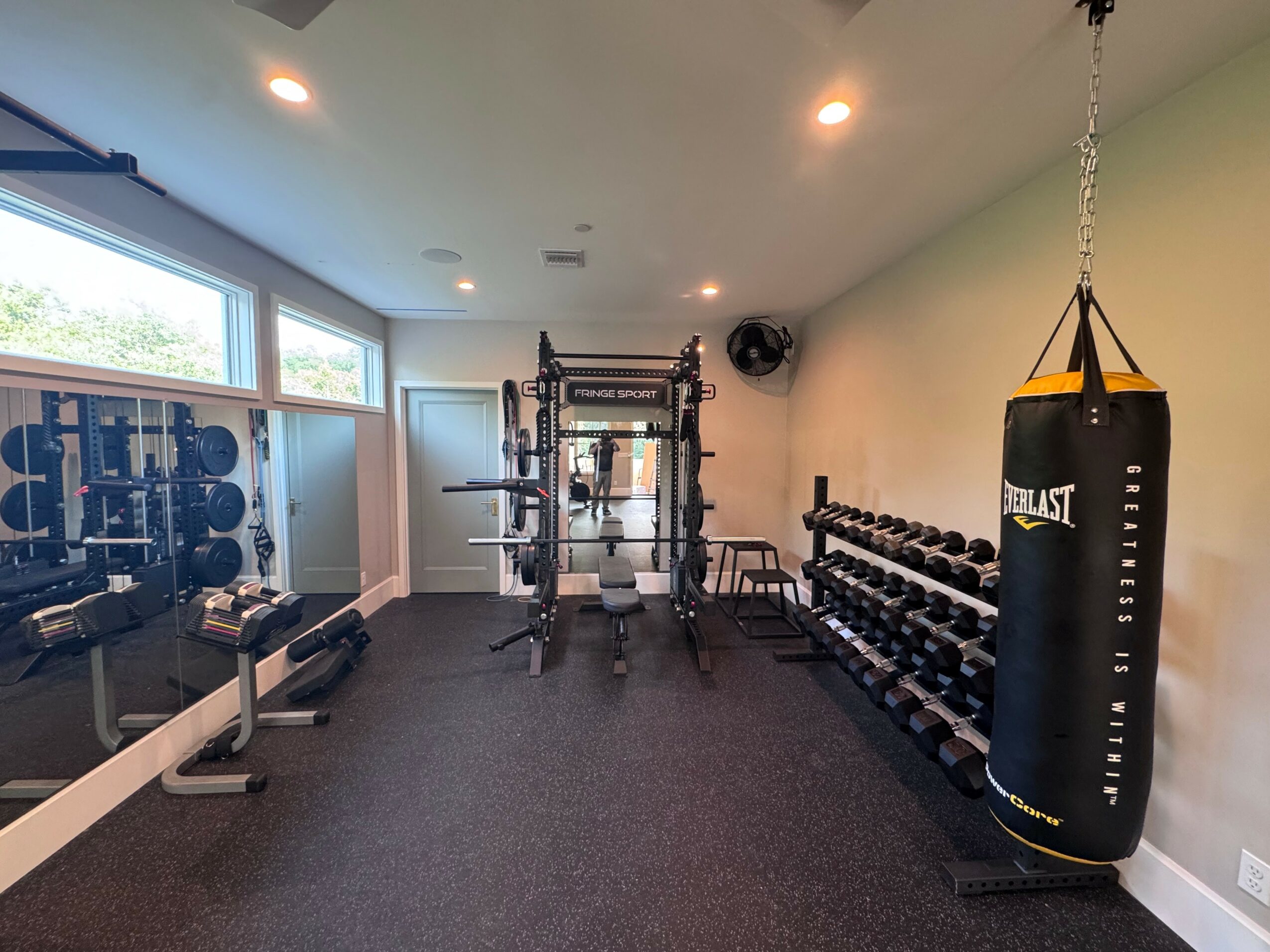 Gym room with weightlifting equipment, punching bag, and large windows, well-lit and organized.