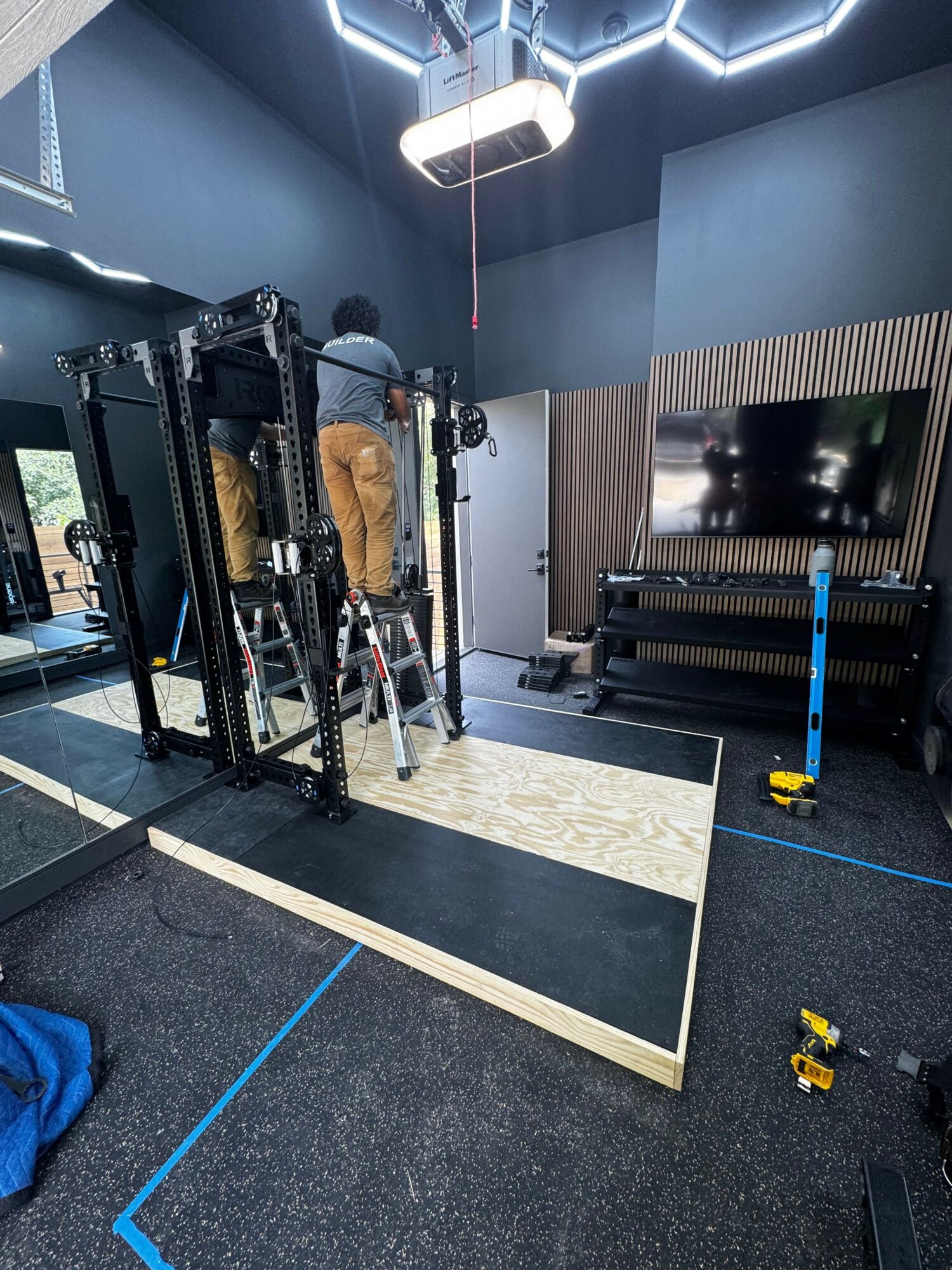 Indoor gym with black metal structure, padded mats, and exercise equipment, illuminated by modern ceiling lights.