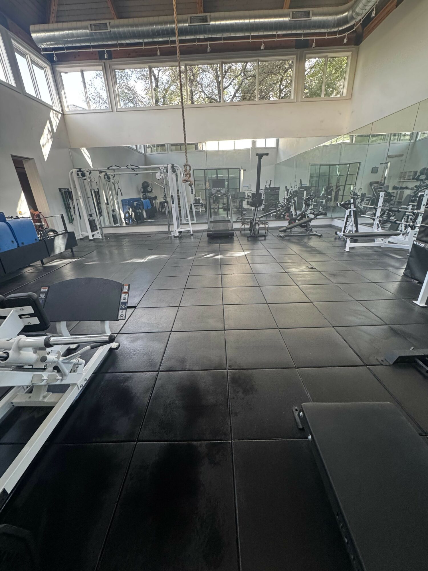 Gym with exercise equipment, large windows, and black tiled floor, viewed from an angle.