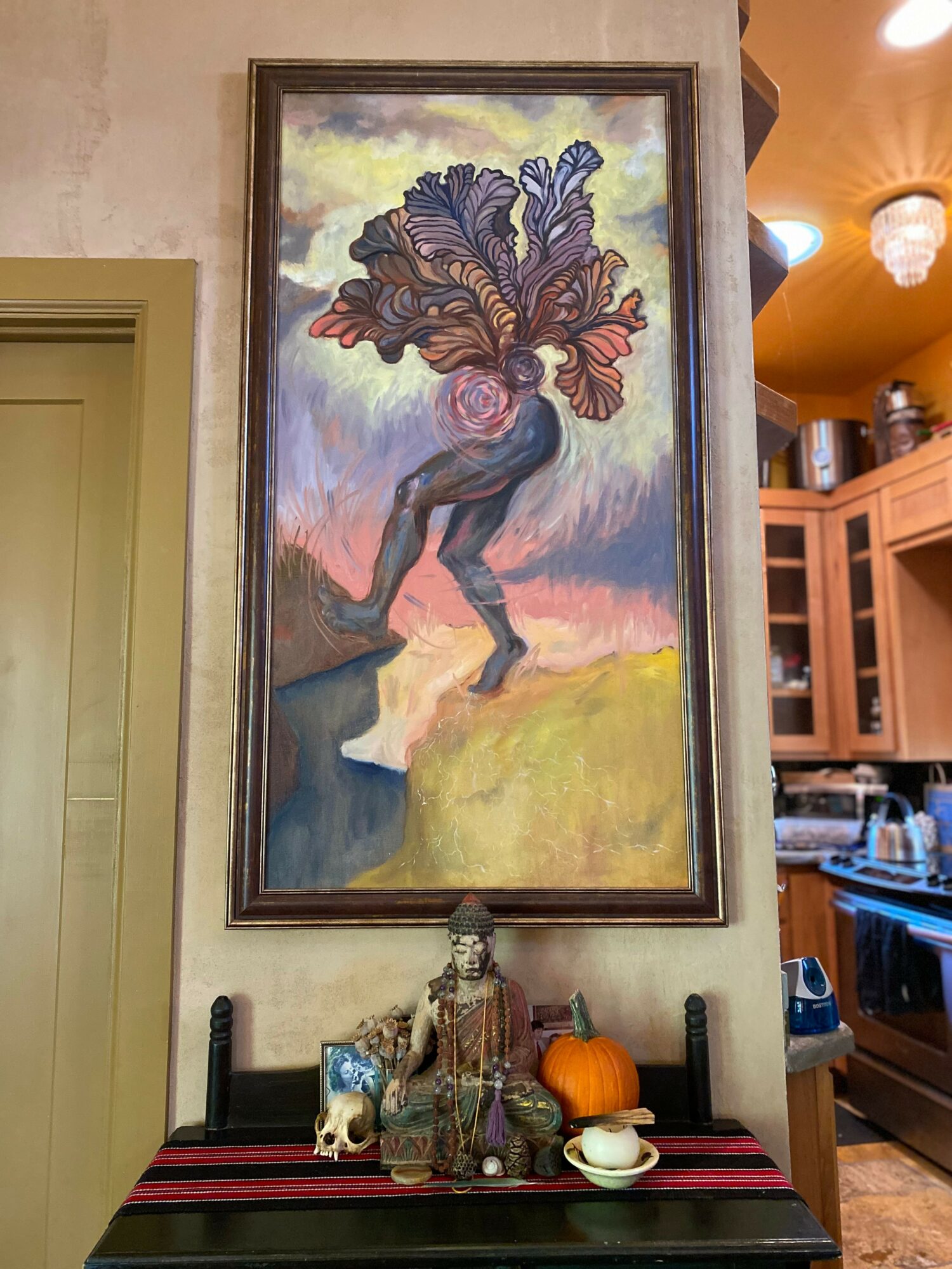 Tall framed painting of a person with a large, colorful, abstract head, standing on a rock near water, with a landscape background.