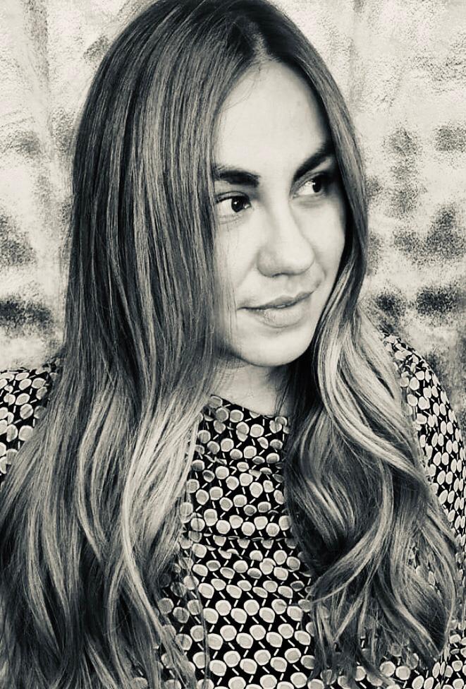 Black and white portrait of a woman with long wavy hair, looking to the side, wearing a patterned top.