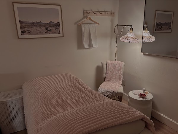 Bedroom with bed, chair, wall art, and a small table, decorated in soft pastel tones.