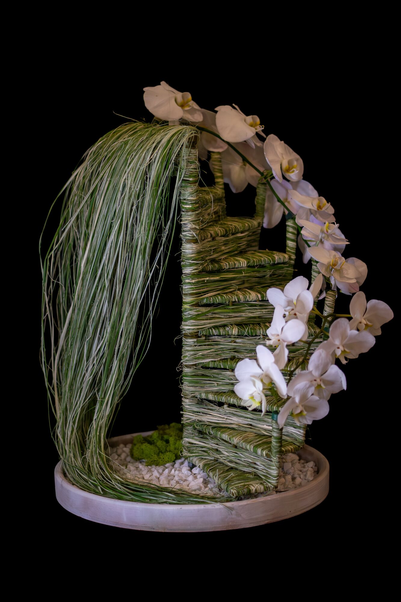 A decorative plant arrangement with cascading green leaves and white flowers on a circular base.